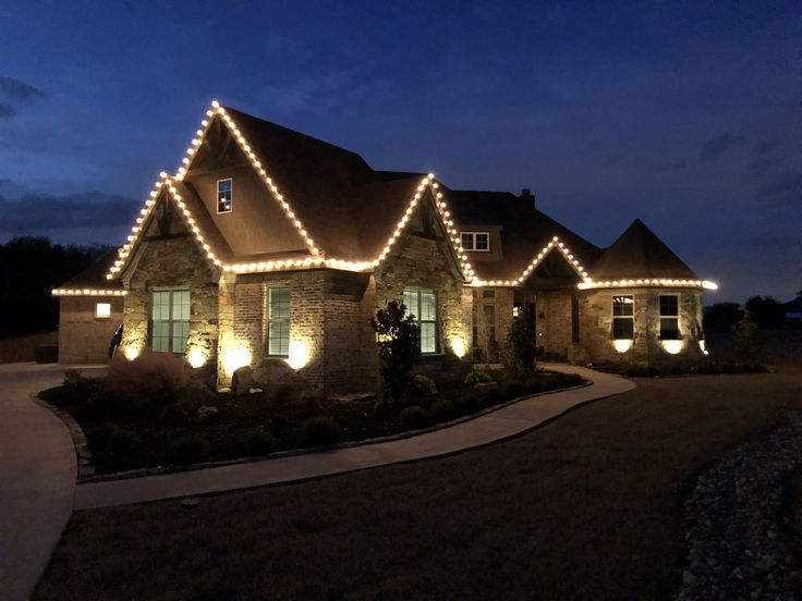 Stone home outlined in warm C9 Christmas lights with landscape uplighting at dusk