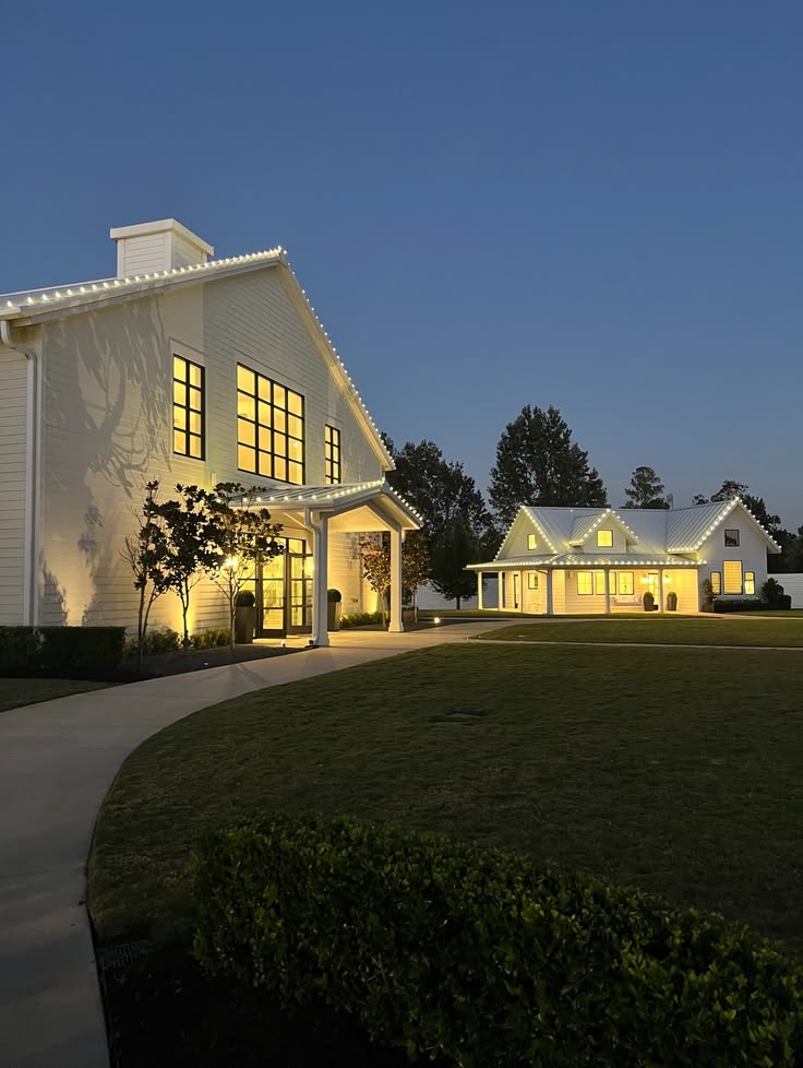 White farmhouse with warm permanent roofline lighting at dusk