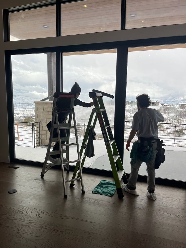 Two Digii technicians cleaning a floor-to-ceiling interior window wall with mountain views