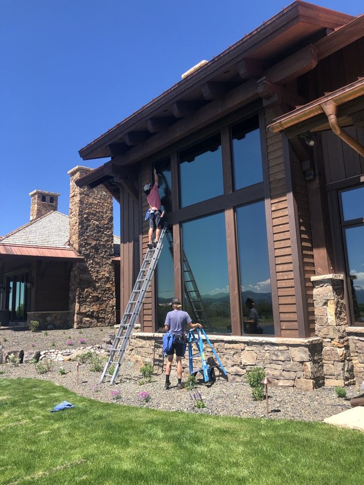Digii Window Cleaning technician cleaning tall exterior windows on a large Colorado Springs home with ladders and professional squeegees